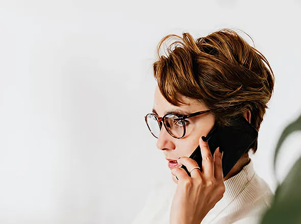 Person with short brown hair and glasses talking on a phone against a white background.